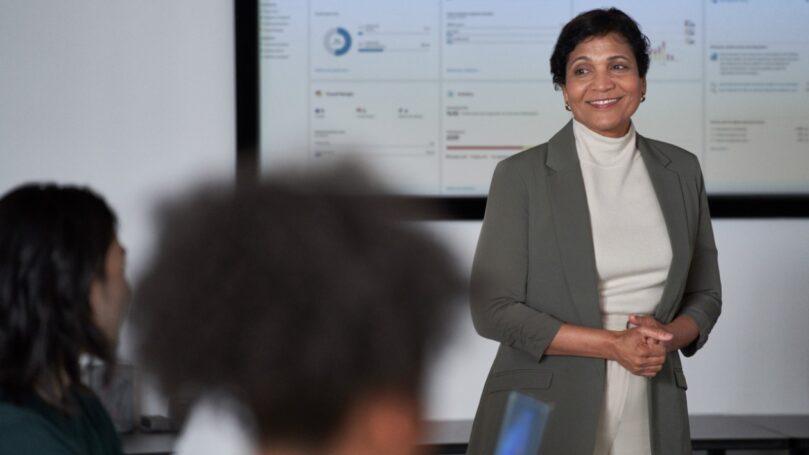 A woman in a suit standing in front of a large screen